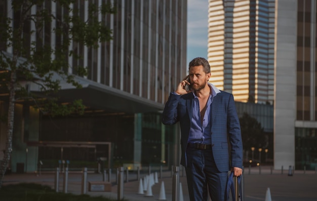 Portrait d'un homme d'affaires mature confiant utilisant un smartphone debout à l'extérieur du bureau