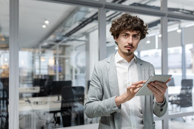 Portrait d'un homme d'affaires mature sérieux pensant avec un ordinateur tablette dans les mains en regardant la caméra