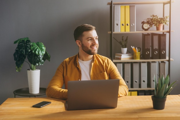 Photo portrait d'un homme d'affaires moderne en chemise jaune travaillant sur un ordinateur portable dans le bureau