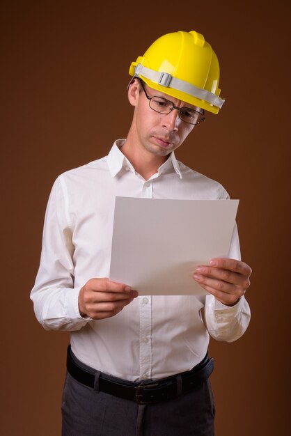 Portrait d'homme d'affaires portant un casque contre un mur marron