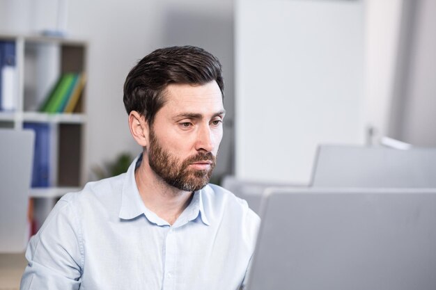 Portrait d'un homme d'affaires prospère et sérieux, pensif, regardant la caméra travaillant au bureau à l'ordinateur