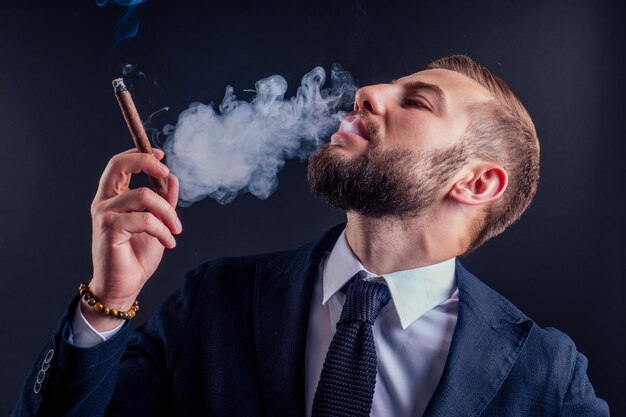 Portrait d'un homme d'affaires séduisant avec un cigare en studio sur fond noir