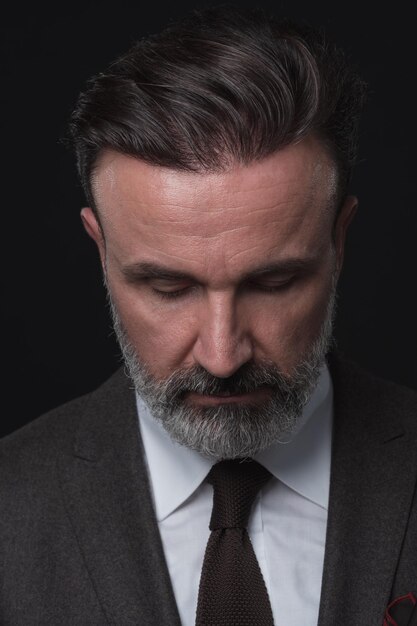 Portrait d'un homme d'affaires senior élégant et élégant avec une barbe et des vêtements d'affaires décontractés en studio photo isolé sur fond sombre gesticulant avec les mains. Photo de haute qualité