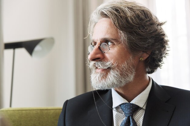 Portrait d'un homme d'affaires senior sérieux et sérieux aux cheveux gris à l'intérieur à la maison vêtu de vêtements formels portant des lunettes.