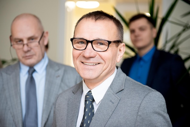 Photo portrait d'un homme d'affaires senior souriant et confiant debout avec des membres de l'équipe en arrière-plan