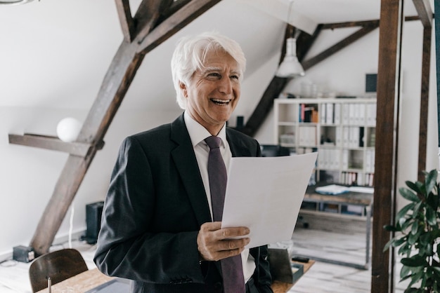 Portrait d'un homme d'affaires senior souriant avec un document dans son bureau