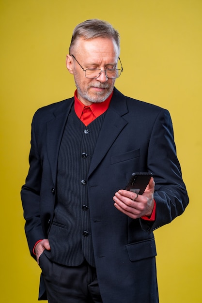 Portrait d'homme d'affaires senior tenant dans les mains téléphone en se tenant debout au studio