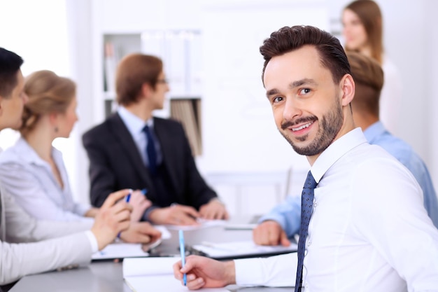 Portrait d'un homme d'affaires souriant et joyeux contre un groupe de personnes lors d'une réunion.