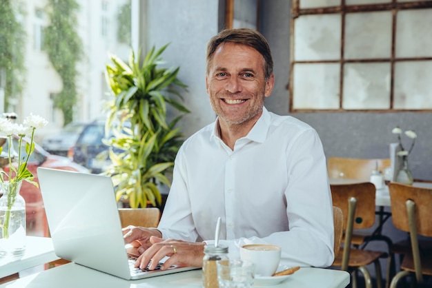 Portrait d'un homme d'affaires souriant travaillant dans un café avec un ordinateur portable