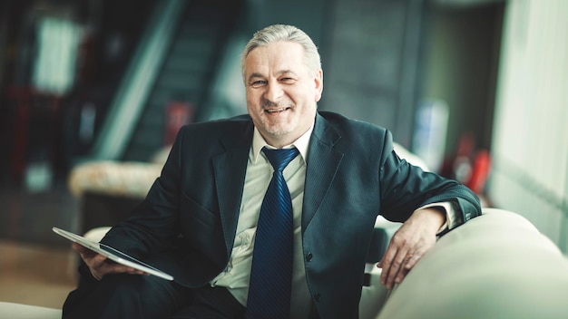 Portrait d'homme d'affaires avec tablette numérique assis sur la chaise devant le bureau