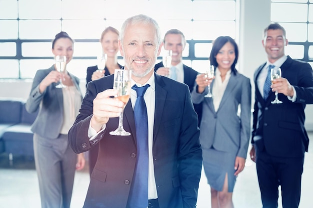 Portrait d'homme d'affaires tenant une flûte à champagne et son équipe debout en arrière-plan