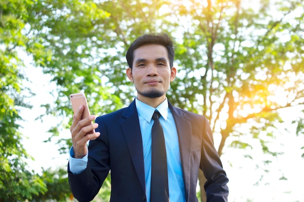 Photo portrait d'un homme d'affaires tenant un téléphone portable alors qu'il se tient contre un arbre