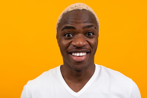 Portrait d'un homme africain charismatique souriant souriant dans un t-shirt blanc sur un fond de studio jaune