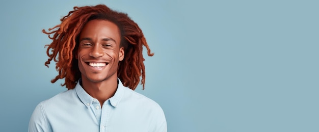 Photo portrait d'un homme africain élégant, sexy et souriant avec une peau sombre parfaite, des cheveux longs rouges sur un bleu clair.