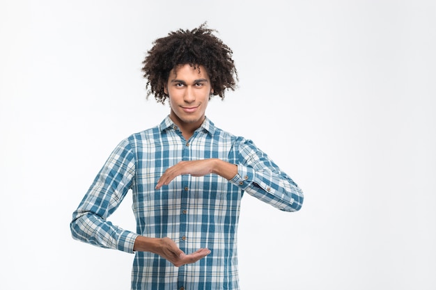 Portrait d'un homme afro-américain décontracté et heureux tenant quelque chose d'invisible isolé sur un mur blanc