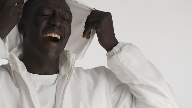 Portrait d'un homme afro-américain élégant et attrayant portant une capuche posant joyeusement devant la caméra sur fond blanc