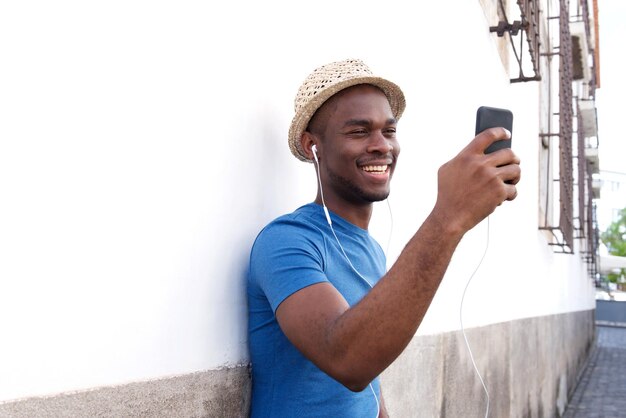 Portrait d'un homme afro-américain heureux, écoutant de la musique avec un téléphone portable et des écouteurs