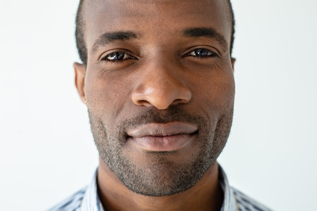 Portrait d'homme afro-américain intelligent vous regardant en se tenant debout contre un mur blanc