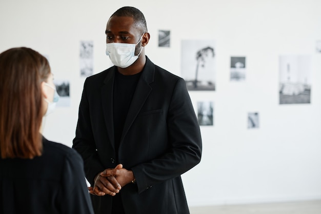 Portrait d'un homme afro-américain portant un masque tout en discutant d'art avec une femme dans une galerie moderne, espace pour copie