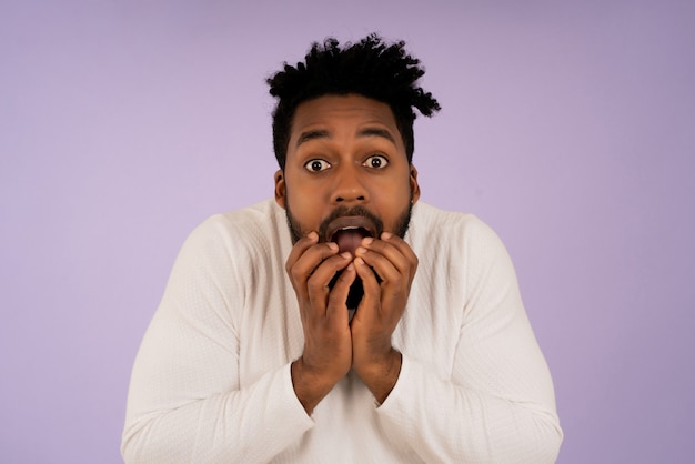 Portrait d'un homme afro effrayé mettant les mains sur sa bouche sur fond isolé.