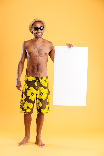 Portrait d'un homme afro heureux tenant un tableau blanc et montrant le signe correct isolé sur un mur orange