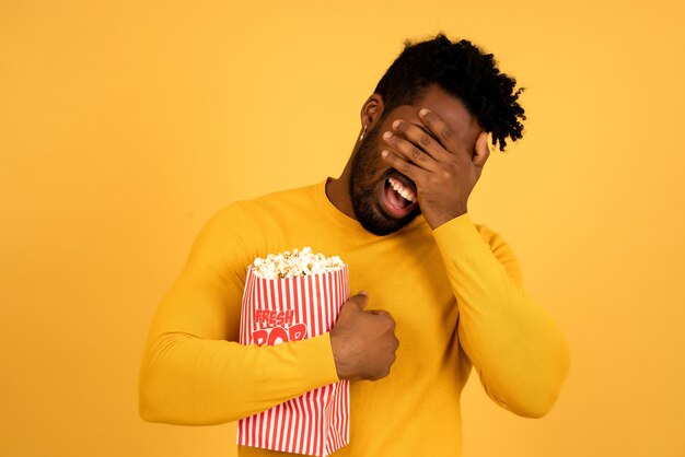 Portrait d'un homme afro mangeant du pop-corn en regardant des films sur fond isolé.