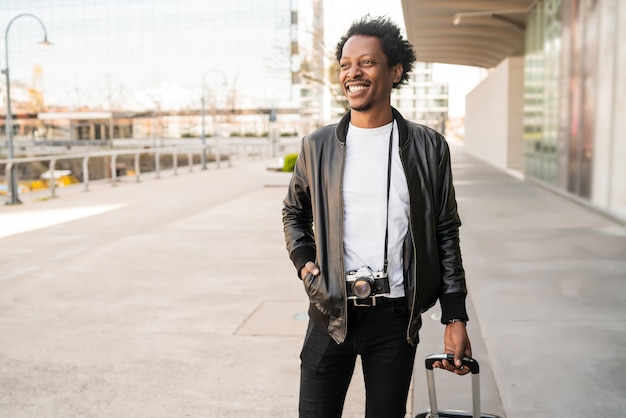 Portrait d'un homme afro touriste portant valise tout en marchant à l'extérieur dans la rue