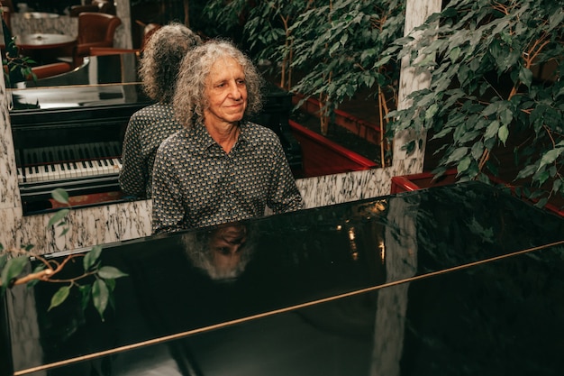 Portrait d'un homme âgé de 60 à 65 ans, cheveux gris bouclés, assis au piano et jouant un morceau de musique, concentré, mélodie injoing