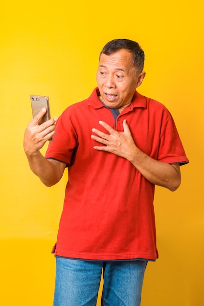 Portrait d'un homme âgé asiatique surpris regardant un téléphone intelligent et étant choqué de grands yeux et de la main sur