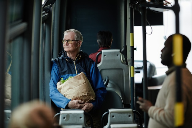 Portrait d'un homme âgé aux cheveux blancs regardant la fenêtre dans un bus lors d'un voyage en transports en commun en ville, espace pour copie