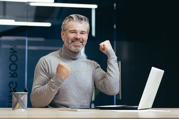 Portrait d'un homme âgé aux cheveux gris qui a réussi un homme heureux est assis au bureau à la table