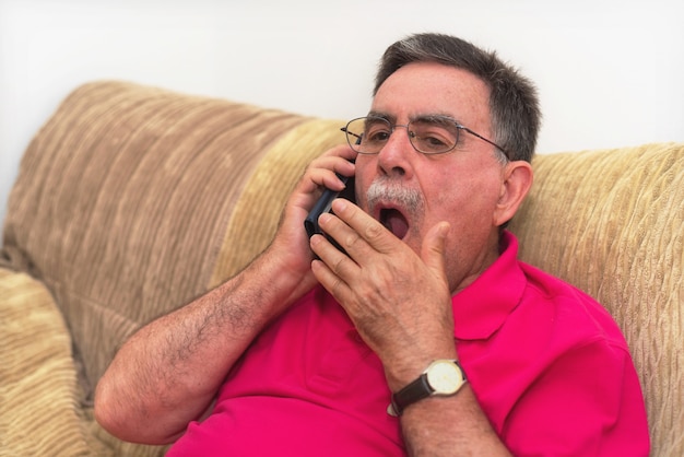 Portrait d&#39;un homme âgé baillant, parlant au téléphone. Conversation ennuyeuse