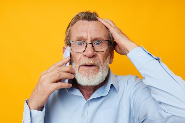 Portrait homme âgé barbe grise avec des lunettes parlant au téléphone fond jaune