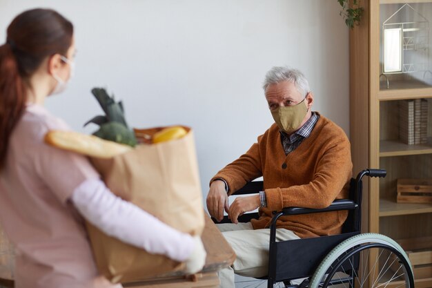 Portrait d'un homme âgé en fauteuil roulant portant un masque tout en acceptant la livraison de nourriture, le concept d'aide et d'assistance, espace de copie