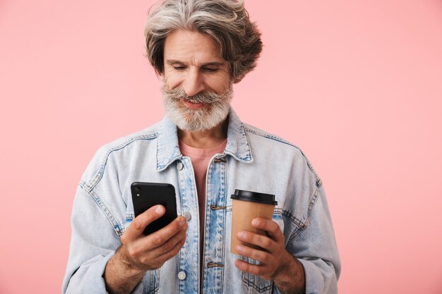 Portrait d'un homme d'âge moyen portant une tenue décontractée, isolé, utilisant un téléphone portable tout en tenant une tasse de café à emporter