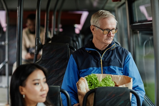 Portrait D'un Homme âgé Regardant La Fenêtre D'un Bus Lors D'un Voyage En Transports En Commun Et Tenant Du Papier...