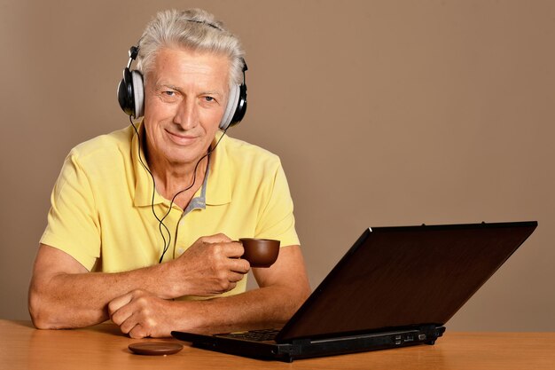 Portrait d'un homme âgé souriant assis à table avec un ordinateur portable