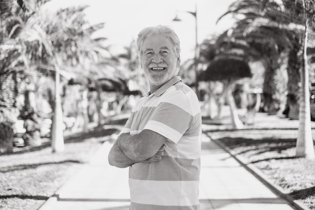 Portrait d'un homme âgé souriant en plein air dans un parc public avec les bras croisés regardant la caméra détendu homme barbu âgé profitant de la liberté et de la retraite