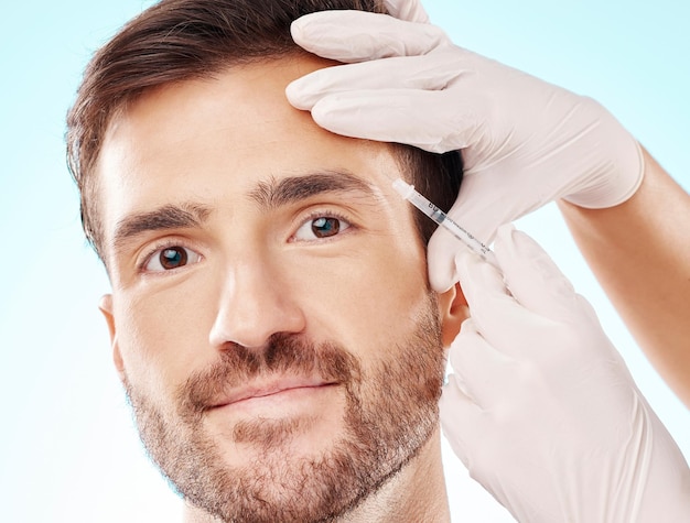 Portrait homme et aiguille pour cosmétiques dermatologie et beauté sur fond de studio bleu Visage homme et homme avec injection de soins de la peau et chirurgie plastique avec gants de botox et changement facial