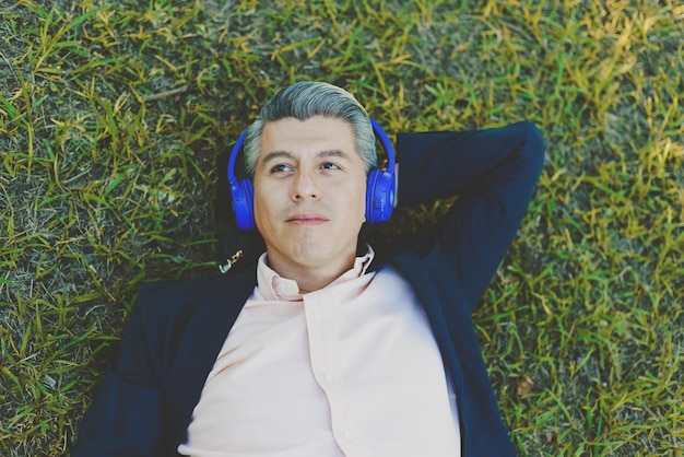 Portrait d'un homme allongé sur l'herbe écoutant de la musique avec des écouteurs