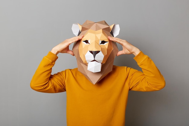 Portrait d'un homme anonyme malsain portant un masque de lion et un sweat-shirt orange isolé sur fond gris ayant des maux de tête garde la main sur la tête souffrant de douleur étant fatigué