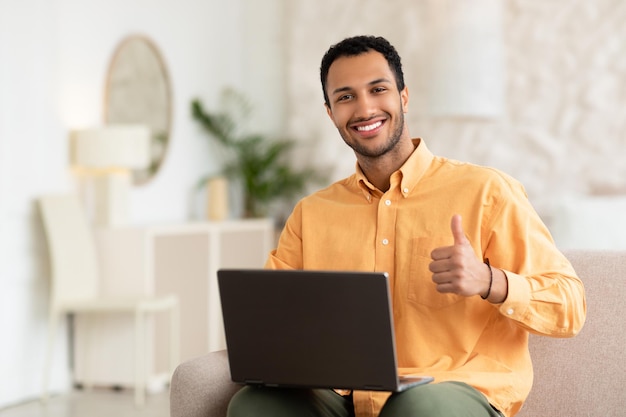 Portrait d'un homme arabe souriant à l'aide d'un ordinateur portable montrant les pouces vers le haut