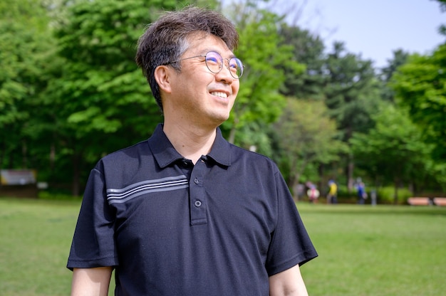 Portrait d'un homme asiatique d'âge moyen souriant sur la pelouse portant un T-shirt.