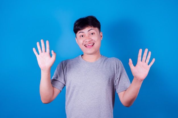 Portrait d'un homme asiatique drôle en t-shirt gris souriant sur fond bleu