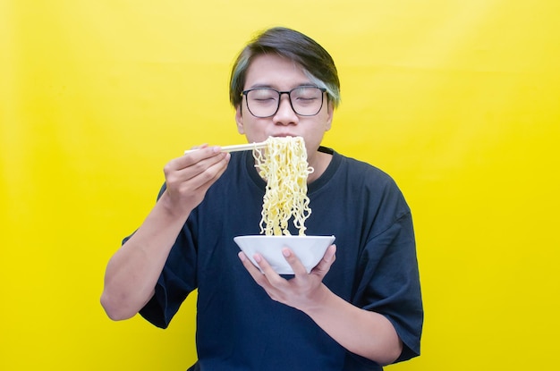 Portrait d'un homme asiatique heureux en t-shirt noir mange des nouilles instantanées à l'aide de baguettes et d'un bol isolés