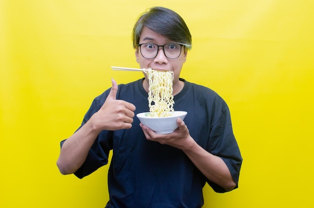 Portrait d'un homme asiatique heureux en t-shirt noir mange des nouilles instantanées à l'aide de baguettes et d'un bol isolés