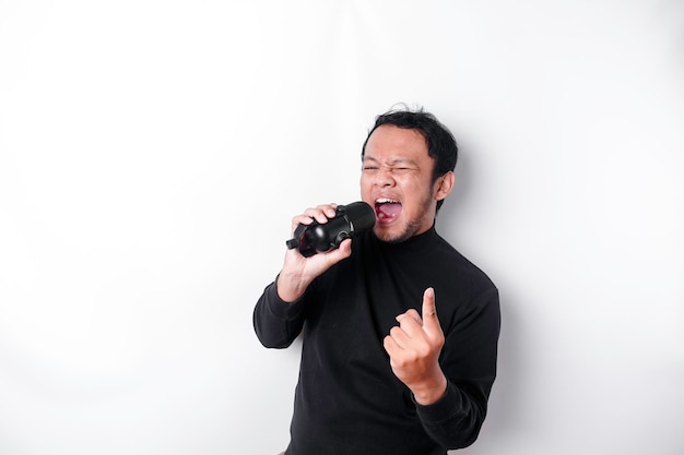 Portrait d'un homme asiatique insouciant s'amusant à chanter au karaoké dans un microphone en se tenant debout sur fond blanc