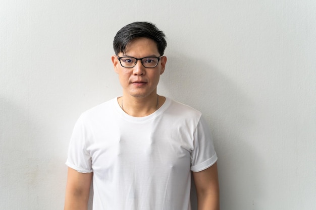 Portrait homme asiatique avec des lunettes regardant la caméra debout sur fond de mur blanc isolé