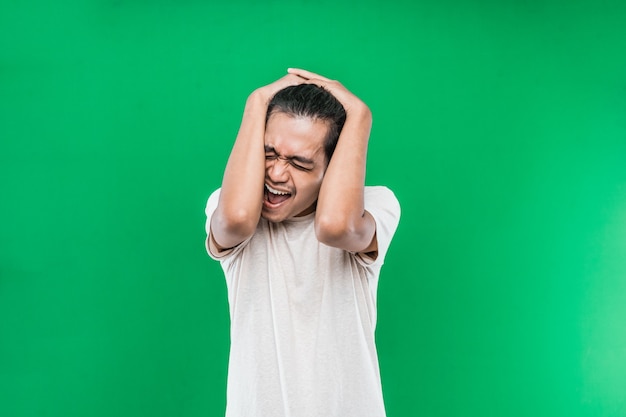 Portrait d'un homme asiatique avec des maux de tête hurlant tenant sa tête sur un fond vert