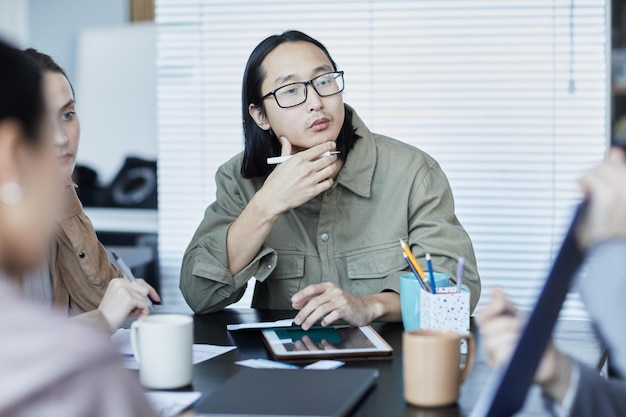 Portrait d'un homme asiatique pensif en réunion d'affaires avec un groupe de personnes discutant d'un projet au bureau